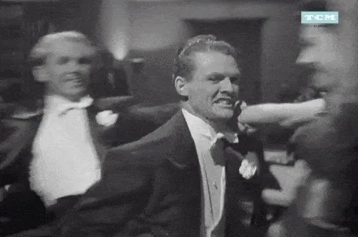 Black-and-white film still of men in tuxedos dancing at a party